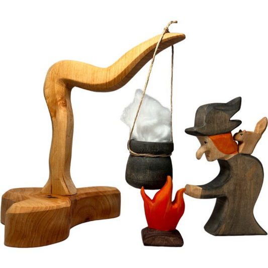 Handgefertigte Holzfiguren für Kinder, Hexe mit Katze auf dem Buckel steht an ihrem Kessel, der von einem Baum hängt. Darunter knistert das Feuer.